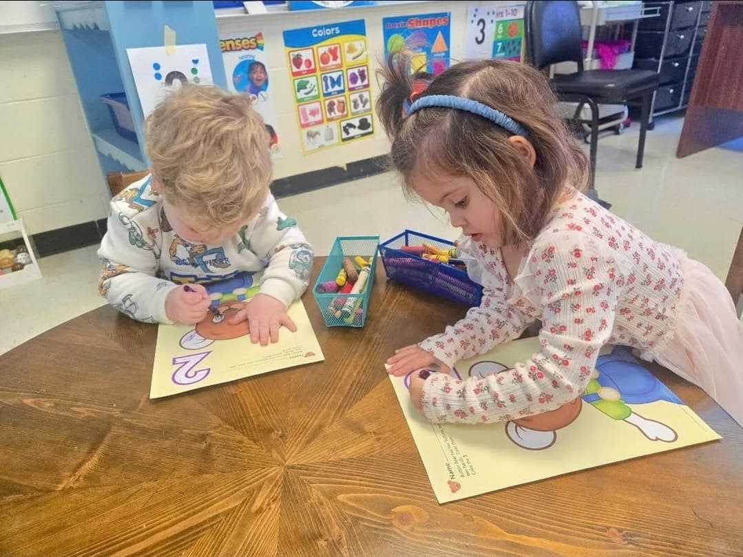 Two preschoolers coloring together at a classroom table